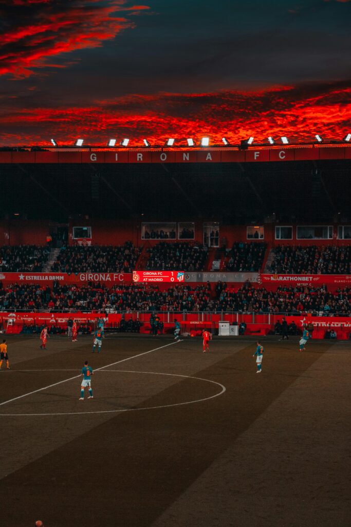 Dramatic evening soccer game at Girona FC stadium with vibrant red sky and intense play.